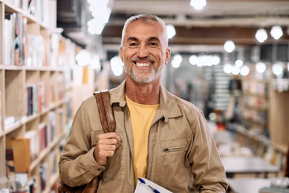 An older gentleman standing in a library, smiling.